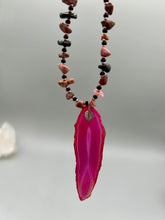Load image into Gallery viewer, Unlock your inner goddess with this stunning Large Fuchsia Agate Geode Sliced Stone Chip Necklace. Featuring a vibrant fuchsia agate geode pendant surrounded by Rhodonite stone chips and gold and black glass beading, the silver leaf bail completes this chic and boho-inspired look. Make a bold statement with this bohemian-style gemstone necklace. Measurements: Necklace is 17 3/4” in length - pendant is 3” Height