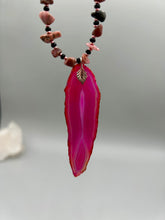 Load image into Gallery viewer, Unlock your inner goddess with this stunning Large Fuchsia Agate Geode Sliced Stone Chip Necklace. Featuring a vibrant fuchsia agate geode pendant surrounded by Rhodonite stone chips and gold and black glass beading, the silver leaf bail completes this chic and boho-inspired look. Make a bold statement with this bohemian-style gemstone necklace. Measurements: Necklace is 17 3/4” in length - pendant is 3” Height