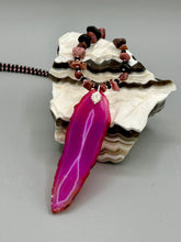 Load image into Gallery viewer, Unlock your inner goddess with this stunning Large Fuchsia Agate Geode Sliced Stone Chip Necklace. Featuring a vibrant fuchsia agate geode pendant surrounded by Rhodonite stone chips and gold and black glass beading, the silver leaf bail completes this chic and boho-inspired look. Make a bold statement with this bohemian-style gemstone necklace. Measurements: Necklace is 17 3/4” in length - pendant is 3” Height