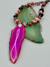 Load image into Gallery viewer, Unlock your inner goddess with this stunning Large Fuchsia Agate Geode Sliced Stone Chip Necklace. Featuring a vibrant fuchsia agate geode pendant surrounded by Rhodonite stone chips and gold and black glass beading, the silver leaf bail completes this chic and boho-inspired look. Make a bold statement with this bohemian-style gemstone necklace. Measurements: Necklace is 17 3/4” in length - pendant is 3” Height