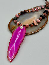 Load image into Gallery viewer, Unlock your inner goddess with this stunning Large Fuchsia Agate Geode Sliced Stone Chip Necklace. Featuring a vibrant fuchsia agate geode pendant surrounded by Rhodonite stone chips and gold and black glass beading, the silver leaf bail completes this chic and boho-inspired look. Make a bold statement with this bohemian-style gemstone necklace. Measurements: Necklace is 17 3/4” in length - pendant is 3” Height