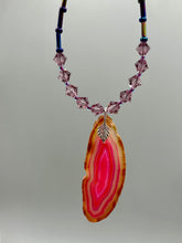 Load image into Gallery viewer, Make a bold style statement with this eye-catching Soft Pink and Amber Agate Geode Sliced Stone Chip Necklace. Featuring a vibrant soft pink and amber tone agate geode pendant surrounded by dark blue glass beads with iridescent tones of purple, blue, green, pink and gold. This bohemian-style gemstone necklace is the perfect way to add a unique touch of shabby boho chic to any look.   Measurements:    Necklace is 18” in length - pendant is 2 1/4” Height