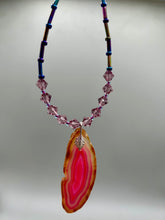 Load image into Gallery viewer, Make a bold style statement with this eye-catching Soft Pink and Amber Agate Geode Sliced Stone Chip Necklace. Featuring a vibrant soft pink and amber tone agate geode pendant surrounded by dark blue glass beads with iridescent tones of purple, blue, green, pink and gold. This bohemian-style gemstone necklace is the perfect way to add a unique touch of shabby boho chic to any look.   Measurements:    Necklace is 18” in length - pendant is 2 1/4” Height