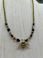 Load image into Gallery viewer, This beautiful Bee Pendant With Black and Yellow Beaded Necklace is the perfect accessory for any summer outfit. The vibrant colors will make a bold statement, while the black and gold blend adds a subtle elegance. Its perfect for any nature lover, hippie, or witchy style.  Measurements:  Necklace is 18”