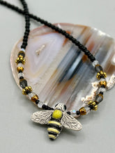 Load image into Gallery viewer, This beautiful Bee Pendant With Black and Yellow Beaded Necklace is the perfect accessory for any summer outfit. The vibrant colors will make a bold statement, while the black and gold blend adds a subtle elegance. Its perfect for any nature lover, hippie, or witchy style.   Measurements:   Necklace is 18”