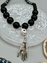 Load image into Gallery viewer, This elegant Peruvian ceramic skull beaded necklace is the perfect accessory for your unique look. With a large skull bead and a lucky hand charm, it exudes a dark, alluring vibe. Complemented with black glass and hematite stone beads, it will make a bold statement. Measurements: Necklace: 19” in length - skulls with lucky hand charm is 2 3/4” Height
