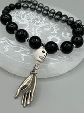 Load image into Gallery viewer, This elegant Peruvian ceramic skull beaded necklace is the perfect accessory for your unique look. With a large skull bead and a lucky hand charm, it exudes a dark, alluring vibe. Complemented with black glass and hematite stone beads, it will make a bold statement. Measurements: Necklace: 19” in length - skulls with lucky hand charm is 2 3/4” Height