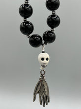 Load image into Gallery viewer, This elegant Peruvian ceramic skull beaded necklace is the perfect accessory for your unique look. With a large skull bead and a lucky hand charm, it exudes a dark, alluring vibe. Complemented with black glass and hematite stone beads, it will make a bold statement. Measurements: Necklace: 19” in length - skulls with lucky hand charm is 2 3/4” Height