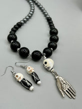 Load image into Gallery viewer, This set of earrings features a mini howlite skull bead with a wood carved black and white bead. Perfect for any goth, emo, witchy, or Day of the Dead outfit, it adds a unique touch to any ensemble. Measurements: 1 1/2 ” in length