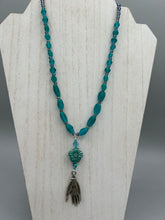 Load image into Gallery viewer, Bring the beauty of nature to your wardrobe with this gorgeous blue-green pressed glass floral beaded necklace. Featuring a large intricate green-blue pressed glass bead, a lucky hand charm, mixed flat matte teal glass beads, and a hook-eye clasp for secure wear, this nature-inspired accessory adds a touch of summer to any outfit. Perfect for day-to-night looks.  Measurements:  Necklace: 19 1/2", Flower and lucky hand pendant 3 1/4"