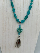 Load image into Gallery viewer, Bring the beauty of nature to your wardrobe with this gorgeous blue-green pressed glass floral beaded necklace. Featuring a large intricate green-blue pressed glass bead, a lucky hand charm, mixed flat matte teal glass beads, and a hook-eye clasp for secure wear, this nature-inspired accessory adds a touch of summer to any outfit. Perfect for day-to-night looks.  Measurements:  Necklace: 19 1/2", Flower and lucky hand pendant 3 1/4"