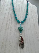 Load image into Gallery viewer, Bring the beauty of nature to your wardrobe with this gorgeous blue-green pressed glass floral beaded necklace. Featuring a large intricate green-blue pressed glass bead, a lucky hand charm, mixed flat matte teal glass beads, and a hook-eye clasp for secure wear, this nature-inspired accessory adds a touch of summer to any outfit. Perfect for day-to-night looks.  Measurements:  Necklace: 19 1/2", Flower and lucky hand pendant 3 1/4"