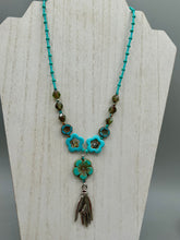 Load image into Gallery viewer, Adorn your look and show your affinity for nature with this exquisite handcrafted necklace, composed of a large intricate sea-green hibiscus pressed glass bead, a lucky hand charm, multiple turquoise, and dark avocado green faceted pressed glass beads, and a hook-eye clasp for secure wear. This nature-inspired statement piece brings warmth to any outfit for both day and night. Measurements:  Necklace: 19 1/2", Flower and lucky hand pendant 3"