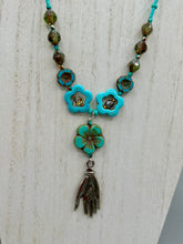 Load image into Gallery viewer, Adorn your look and show your affinity for nature with this exquisite handcrafted necklace, composed of a large intricate sea-green hibiscus pressed glass bead, a lucky hand charm, multiple turquoise, and dark avocado green faceted pressed glass beads, and a hook-eye clasp for secure wear. This nature-inspired statement piece brings warmth to any outfit for both day and night. Measurements:  Necklace: 19 1/2", Flower and lucky hand pendant 3"