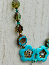 Load image into Gallery viewer, Adorn your look and show your affinity for nature with this exquisite handcrafted necklace, composed of a large intricate sea-green hibiscus pressed glass bead, a lucky hand charm, multiple turquoise, and dark avocado green faceted pressed glass beads, and a hook-eye clasp for secure wear. This nature-inspired statement piece brings warmth to any outfit for both day and night. Measurements:  Necklace: 19 1/2", Flower and lucky hand pendant 3"