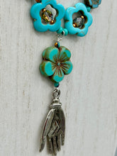 Load image into Gallery viewer, Adorn your look and show your affinity for nature with this exquisite handcrafted necklace, composed of a large intricate sea-green hibiscus pressed glass bead, a lucky hand charm, multiple turquoise, and dark avocado green faceted pressed glass beads, and a hook-eye clasp for secure wear. This nature-inspired statement piece brings warmth to any outfit for both day and night. Measurements:  Necklace: 19 1/2", Flower and lucky hand pendant 3"
