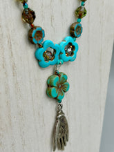 Load image into Gallery viewer, Adorn your look and show your affinity for nature with this exquisite handcrafted necklace, composed of a large intricate sea-green hibiscus pressed glass bead, a lucky hand charm, multiple turquoise, and dark avocado green faceted pressed glass beads, and a hook-eye clasp for secure wear. This nature-inspired statement piece brings warmth to any outfit for both day and night. Measurements:  Necklace: 19 1/2", Flower and lucky hand pendant 3"