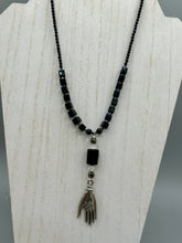 Load image into Gallery viewer, This elegant black obsidian square-shaped beaded necklace is the perfect accessory for your unique look. With a large black bead adorned with multi-color cloisonné bead and a lucky hand charm, it exudes a dark, alluring vibe. Complemented with black glass and hematite stone beads, it will make a bold statement. Measurements: Necklace: 18” in length - lucky hand charm is 3 1 /2” Height