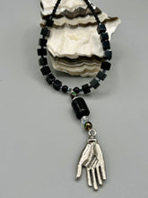 Load image into Gallery viewer, This elegant black obsidian square-shaped beaded necklace is the perfect accessory for your unique look. With a large black bead adorned with multi-color cloisonné bead and a lucky hand charm, it exudes a dark, alluring vibe. Complemented with black glass and hematite stone beads, it will make a bold statement. Measurements: Necklace: 18” in length - lucky hand charm is 3 1 /2” Height