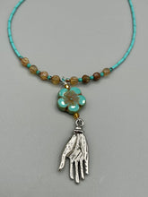 Load image into Gallery viewer, Complete your look with this carefully crafted necklace, featuring a large sea-green hibiscus pressed glass bead, a lucky hand charm, assorted champagne melon beads, and turquoise glass beads. All these elements are combined with a hook-eye clasp, ensuring lasting wear. This nature-inspired accessory adds a touch of charm to all kinds of outfits, making it ideal for both day and night. Measurements: Necklace: 18"