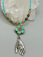 Load image into Gallery viewer, Complete your look with this carefully crafted necklace, featuring a large sea-green hibiscus pressed glass bead, a lucky hand charm, assorted champagne melon beads, and turquoise glass beads. All these elements are combined with a hook-eye clasp, ensuring lasting wear. This nature-inspired accessory adds a touch of charm to all kinds of outfits, making it ideal for both day and night. Measurements: Necklace: 18"