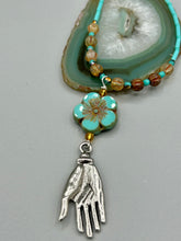 Load image into Gallery viewer, Complete your look with this carefully crafted necklace, featuring a large sea-green hibiscus pressed glass bead, a lucky hand charm, assorted champagne melon beads, and turquoise glass beads. All these elements are combined with a hook-eye clasp, ensuring lasting wear. This nature-inspired accessory adds a touch of charm to all kinds of outfits, making it ideal for both day and night. Measurements: Necklace: 18"