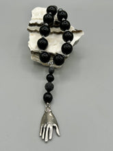 Load image into Gallery viewer, This elegant hematite and black glass beaded necklace is the perfect accessory for your unique look. With a large black and gray glass beads adorned with a lucky hand charm, it exudes a dark, alluring vibe. Complemented with floral shaped metal beads, it will make a bold statement.  Measurements:  Necklace: 18” in length - lucky hand charm is 3 1 /2” Height