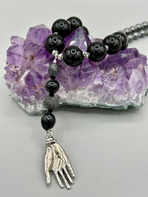 Load image into Gallery viewer, This elegant hematite and black glass beaded necklace is the perfect accessory for your unique look. With a large black and gray glass beads adorned with a lucky hand charm, it exudes a dark, alluring vibe. Complemented with floral shaped metal beads, it will make a bold statement.  Measurements:  Necklace: 18” in length - lucky hand charm is 3 1 /2” Height