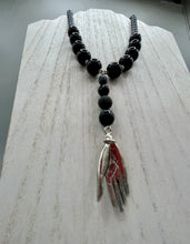 Load image into Gallery viewer, This elegant hematite and black glass beaded necklace is the perfect accessory for your unique look. With a large black and gray glass beads adorned with a lucky hand charm, it exudes a dark, alluring vibe. Complemented with floral shaped metal beads, it will make a bold statement.  Measurements:  Necklace: 18” in length - lucky hand charm is 3 1 /2” Height