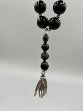 Load image into Gallery viewer, This elegant hematite and black glass beaded necklace is the perfect accessory for your unique look. With a large black and gray glass beads adorned with a lucky hand charm, it exudes a dark, alluring vibe. Complemented with floral shaped metal beads, it will make a bold statement.  Measurements:  Necklace: 18” in length - lucky hand charm is 3 1 /2” Height