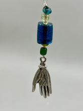 Load image into Gallery viewer, Bring the beauty of nature to your wardrobe with this gorgeous blue-green glass beaded necklace. Featuring a large rectangular blue-green glass bead, a lucky hand charm, mixed flat matte teal glass beads, and a hook-eye clasp for secure wear, this nature-inspired accessory adds a touch of summer to any outfit. Perfect for day-to-night looks.   Measurements:  Necklace: 19", Lucky hand pendant 3 1/2"