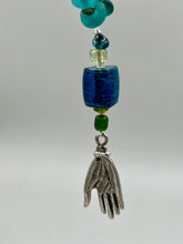 Load image into Gallery viewer, Bring the beauty of nature to your wardrobe with this gorgeous blue-green glass beaded necklace. Featuring a large rectangular blue-green glass bead, a lucky hand charm, mixed flat matte teal glass beads, and a hook-eye clasp for secure wear, this nature-inspired accessory adds a touch of summer to any outfit. Perfect for day-to-night looks.   Measurements:  Necklace: 19", Lucky hand pendant 3 1/2"