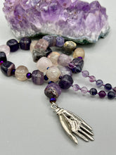Load image into Gallery viewer, This nature-inspired accessory features an array of unique hues, including rainbow fluorite stone beads and iridescent dark shimmery purple glass beads with hints of gold, blue, pink, and green. The secure hook-eye clasp makes it perfect for day to night wear, allowing you to add a touch of summer to your wardrobe. The necklace is further complemented by a large square-shaped rainbow fluorite bead and a lucky hand charm. Measurements: Necklace: 18", Lucky hand pendant 3"