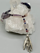 Load image into Gallery viewer, This nature-inspired accessory features an array of unique hues, including rectangular-shaped rainbow fluorite stone beads, round amethyst beads and dark purple glass beads. The secure hook-eye clasp makes it perfect for day to night wear, allowing you to add a touch of summer to your wardrobe. The necklace is further complemented by a large square-shaped rainbow fluorite bead and a lucky hand charm. Measurements: Necklace: 18", Lucky hand pendant 3"