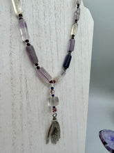 Load image into Gallery viewer, This nature-inspired accessory features an array of unique hues, including rectangular-shaped rainbow fluorite stone beads, round amethyst beads and dark purple glass beads. The secure hook-eye clasp makes it perfect for day to night wear, allowing you to add a touch of summer to your wardrobe. The necklace is further complemented by a large square-shaped rainbow fluorite bead and a lucky hand charm. Measurements: Necklace: 18", Lucky hand pendant 3"