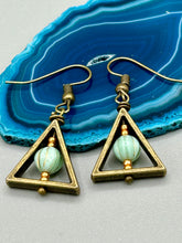 Load image into Gallery viewer, Antique antique brass plated steel ear-wire French Hook Earrings. Antique brass triangle dangle earrings feature a light mint green melon Czech faceted round glass beads with a tint of light gold shimmer. Unique style earrings display a beautiful complimentary tones between the light mint green beads and the warm brass tone. Antique antique brass plated steel ear-wire French Hook Earrings. Measurements: 1" length