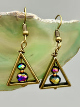 Load image into Gallery viewer, Antique brass triangle dangle earrings feature a purple tone glass bead with an iridescent shimmer finish showcasing hues of gold, purple, blue and pink. Unique style earrings display a beautiful contras between the dark and cool tone glass beads and the warm brass tone. Antique brass plated steel ear-wire French Hook Earrings. Measurements: 1" length