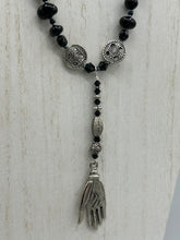 Load image into Gallery viewer, This sophisticated onyx beaded necklace features a large lucky hand charm adorned with floral metal beads, conveying an enchanting aura. The piece is finished with long black glass and floral metal beaded hanging strands, creating a bold and engaging visual statement. Measurements:  Necklace: 19” in length - lucky hand charm is 4” Height