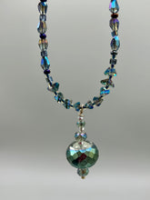 Load image into Gallery viewer, Make a bold statement with this shimmery aqua blue and blue tones glass beaded necklace. The round faceted shaped pendant compliments the cool tones of the necklace, perfect for adding a rich pop of color to any Spring outfit. The draped design gives this piece an elegant, bohemian look. Measurements: Necklace is 18” in length, pendant is 1 1/2”