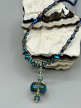 Load image into Gallery viewer, Make a bold statement with this shimmery aqua blue and blue tones glass beaded necklace. The round faceted shaped pendant compliments the cool tones of the necklace, perfect for adding a rich pop of color to any Spring outfit. The draped design gives this piece an elegant, bohemian look. Measurements: Necklace is 18” in length, pendant is 1 1/2”