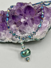 Load image into Gallery viewer, Make a bold statement with this shimmery aqua blue and blue tones glass beaded necklace. The round faceted shaped pendant compliments the cool tones of the necklace, perfect for adding a rich pop of color to any Spring outfit. The draped design gives this piece an elegant, bohemian look. Measurements: Necklace is 18” in length, pendant is 1 1/2”