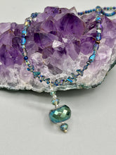 Load image into Gallery viewer, Make a bold statement with this shimmery aqua blue and blue tones glass beaded necklace. The round faceted shaped pendant compliments the cool tones of the necklace, perfect for adding a rich pop of color to any Spring outfit. The draped design gives this piece an elegant, bohemian look. Measurements: Necklace is 18” in length, pendant is 1 1/2”