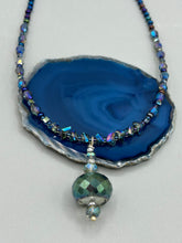 Load image into Gallery viewer, Make a bold statement with this shimmery aqua blue and blue tones glass beaded necklace. The round faceted shaped pendant compliments the cool tones of the necklace, perfect for adding a rich pop of color to any Spring outfit. The draped design gives this piece an elegant, bohemian look. Measurements: Necklace is 18” in length, pendant is 1 1/2”