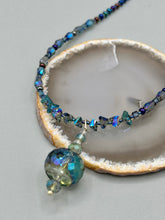 Load image into Gallery viewer, Make a bold statement with this shimmery aqua blue and blue tones glass beaded necklace. The round faceted shaped pendant compliments the cool tones of the necklace, perfect for adding a rich pop of color to any Spring outfit. The draped design gives this piece an elegant, bohemian look. Measurements: Necklace is 18” in length, pendant is 1 1/2”
