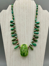 Load image into Gallery viewer, This powerful statement piece necklace features an eye-catching hand sculpted dark blue clay scarab beetle pendant. Adorned with green magnesite and serpentine teintee stone beaded necklace, this dramatic necklace artfully wraps around the neck, conveying an elegant and bold style. Necklace is 20 1/4" in length