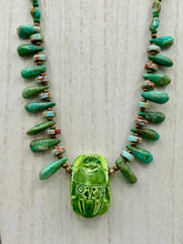 Load image into Gallery viewer, This powerful statement piece necklace features an eye-catching hand sculpted dark blue clay scarab beetle pendant. Adorned with green magnesite and serpentine teintee stone beaded necklace, this dramatic necklace artfully wraps around the neck, conveying an elegant and bold style. Necklace is 20 1/4" in length