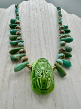Load image into Gallery viewer, This powerful statement piece necklace features an eye-catching hand sculpted dark blue clay scarab beetle pendant. Adorned with green magnesite and serpentine teintee stone beaded necklace, this dramatic necklace artfully wraps around the neck, conveying an elegant and bold style. Necklace is 20 1/4" in length