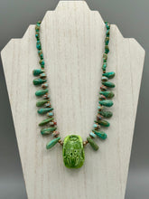 Load image into Gallery viewer, This powerful statement piece necklace features an eye-catching hand sculpted dark blue clay scarab beetle pendant. Adorned with green magnesite and serpentine teintee stone beaded necklace, this dramatic necklace artfully wraps around the neck, conveying an elegant and bold style. Necklace is 20 1/4" in length