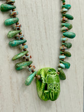Load image into Gallery viewer, This powerful statement piece necklace features an eye-catching hand sculpted dark blue clay scarab beetle pendant. Adorned with green magnesite and serpentine teintee stone beaded necklace, this dramatic necklace artfully wraps around the neck, conveying an elegant and bold style. Necklace is 20 1/4" in length