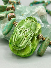 Load image into Gallery viewer, This powerful statement piece necklace features an eye-catching hand sculpted dark blue clay scarab beetle pendant. Adorned with green magnesite and serpentine teintee stone beaded necklace, this dramatic necklace artfully wraps around the neck, conveying an elegant and bold style. Necklace is 20 1/4" in length